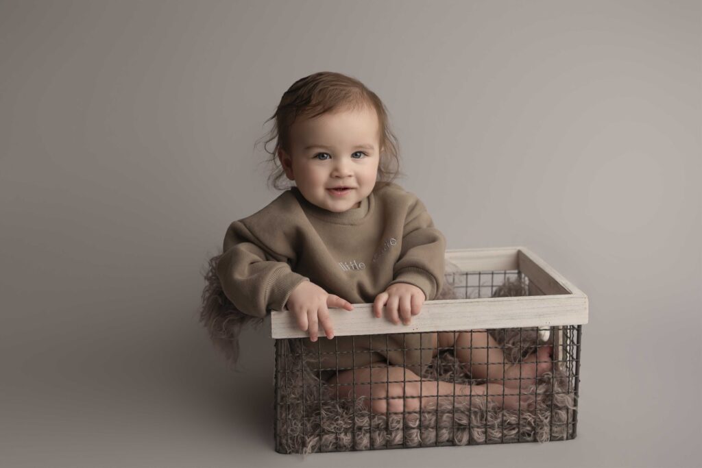 "Smiling baby boy sitting in a rustic wire basket during a studio milestone photo session in Puyallup, WA by Veronica Victoria Photography"
